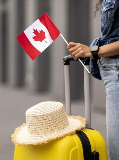 Cropped of woman traveller holding yellow luggage with straw hat on and flag of Canada, going vacation overseas, airport background, copy space. Immigration, education abroad concept