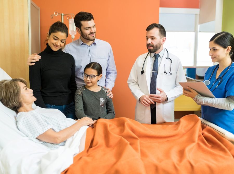 Male and female healthcare workers explaining disease to senior patient with family at hospital